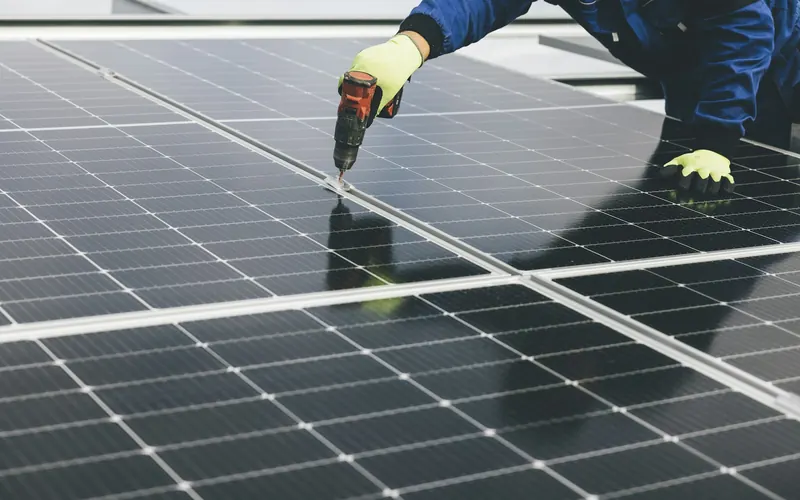 Technician in work gloves fastening a solar panel with a power drill