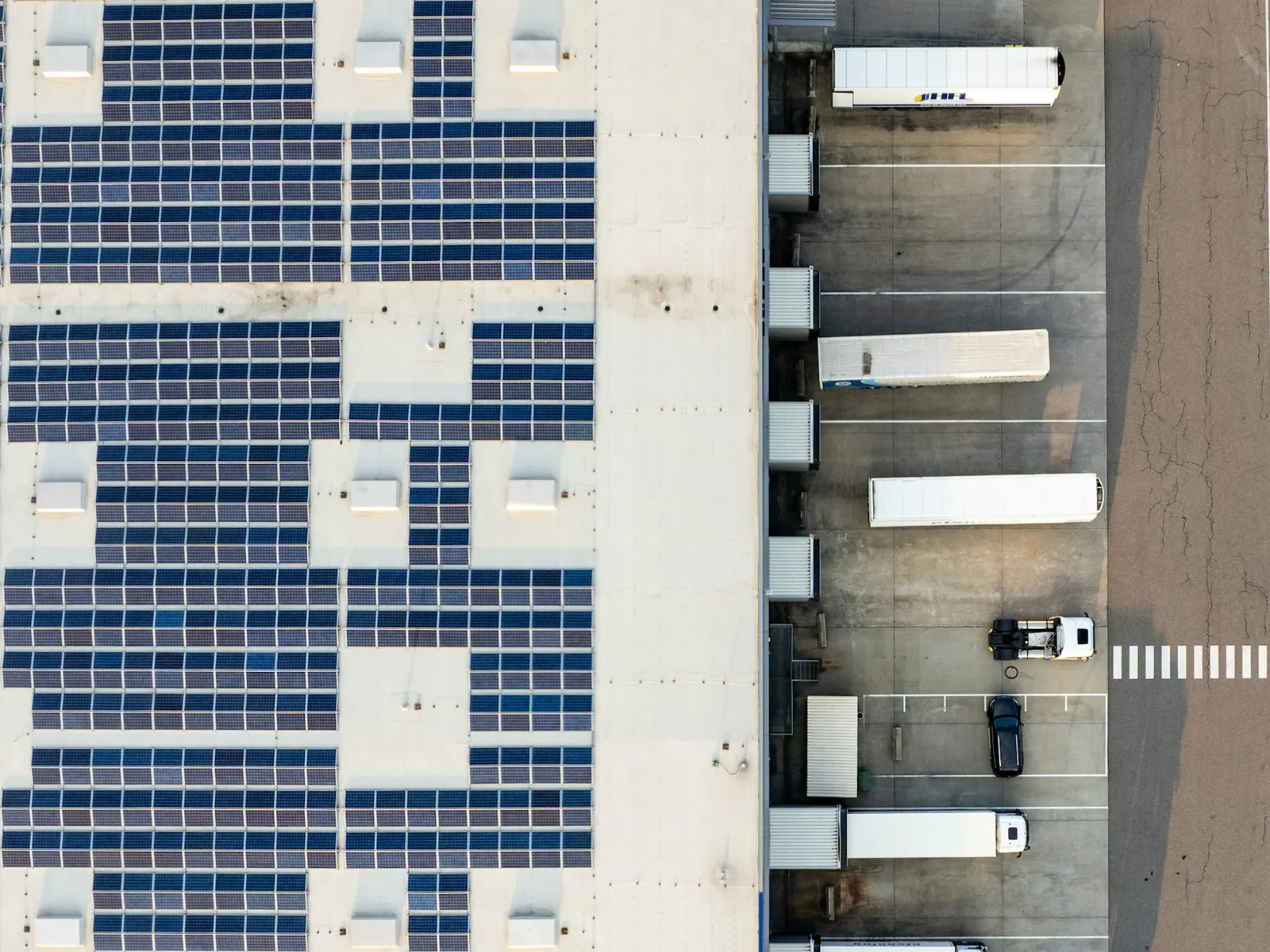 Aerial view of a large warehouse roof covered with rows of solar panels next to a truck loading yard